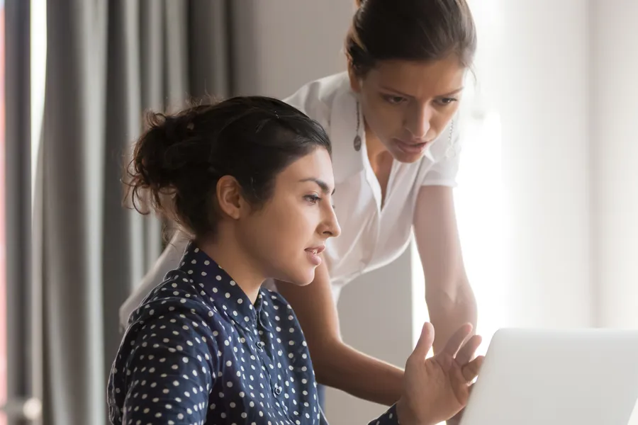 To personer samarbeider foran en bærbar PC, der den ene sitter og peker mot skjermen mens den andre står og gir veiledning