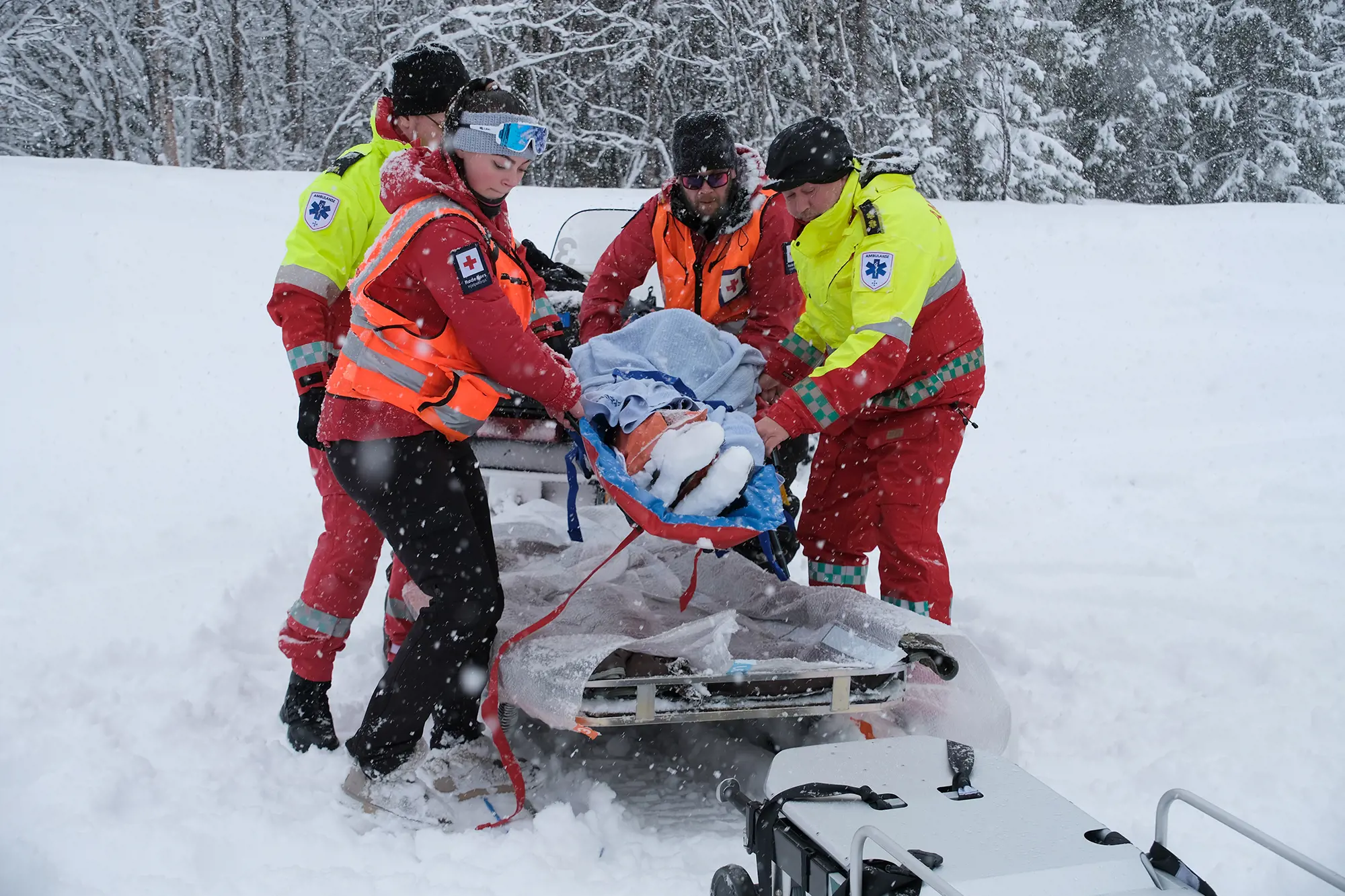 Pasienten på vei med båre fra snøscooteren til ambulansen.