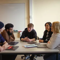 En gruppe på fem elever sitter ved et bord og snakker