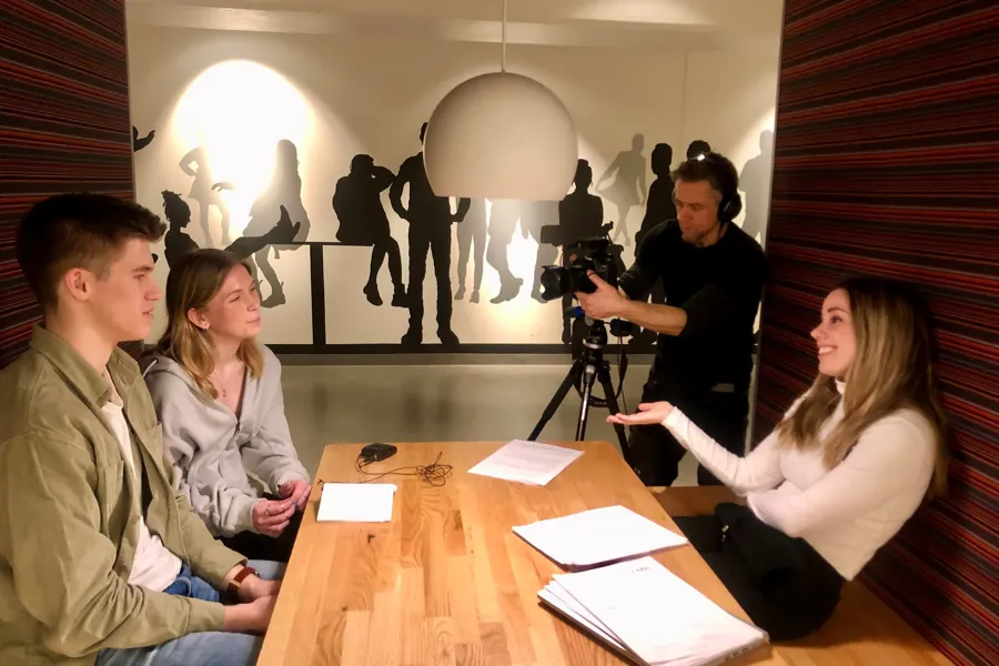 En gruppe mennesker som sitter rundt et bord med en person som står i bakgrunnen