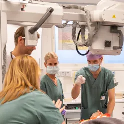 En gruppe mennesker i kirurgiske skrubb som ser på en person i en maske