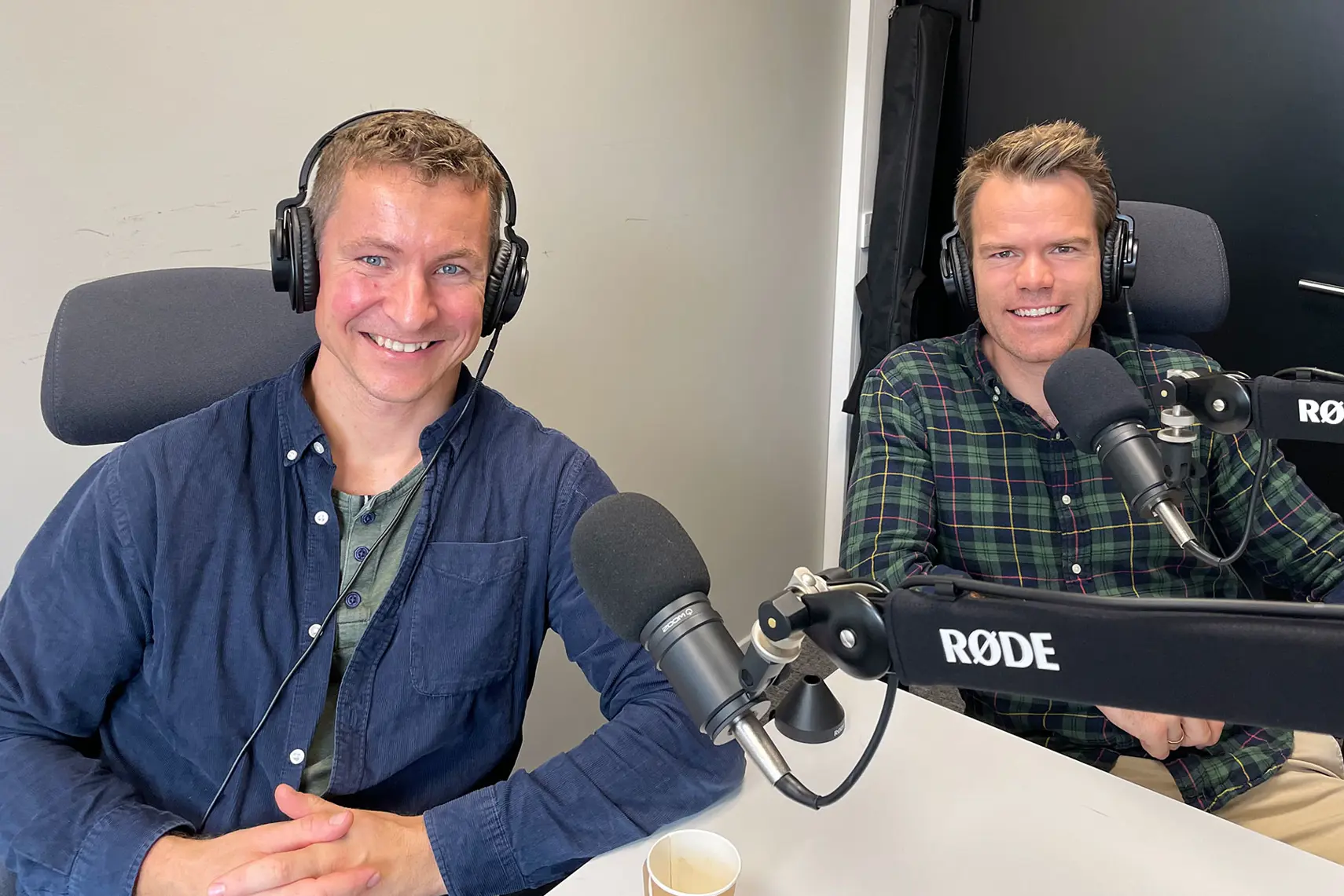 Et par menn som sitter ved et bord med mikrofoner
